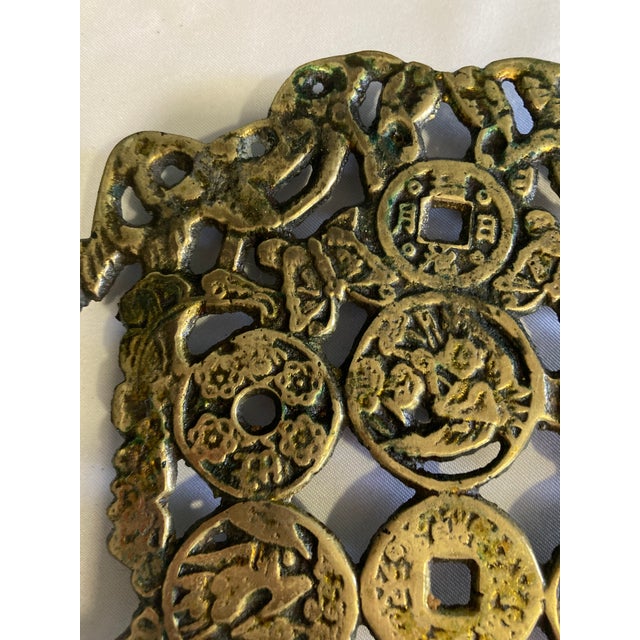 This vintage brass trivet showcases a beautifully detailed composition of traditional Chinese coins and symbolic motifs...