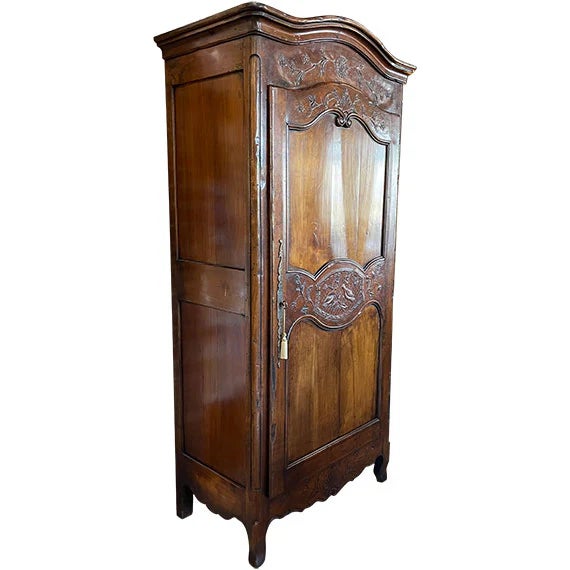 A tall wooden armoire with a richly stained finish and ornate carved detailing across the crown and door panels. The...