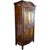 A tall wooden armoire with a richly stained finish and ornate carved detailing across the crown and door panels. The...
