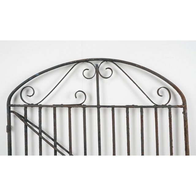 Antique wrought iron garden gate featuring an arched top and decorative scrollwork. Good condition with surface wear,...