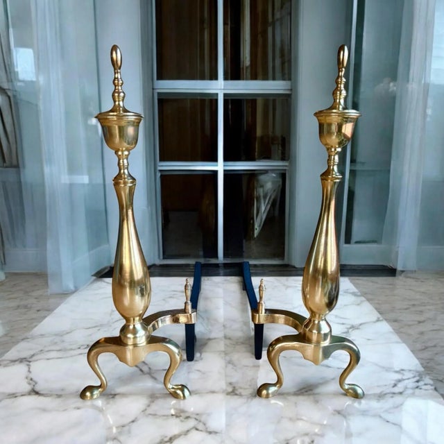 Brass andirons or chenets with 22” tall vertical urn shape and topped finial. These chenets include a brass billet cap...