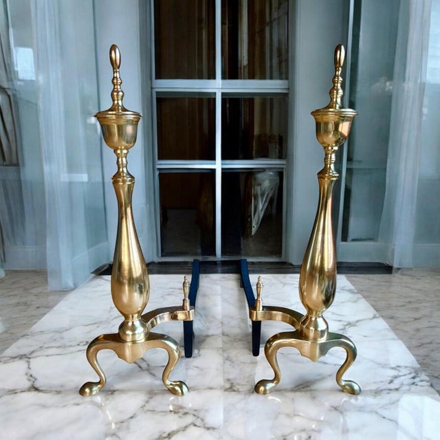 Brass andirons or chenets with 22” tall vertical urn shape and topped finial. These chenets include a brass billet cap...