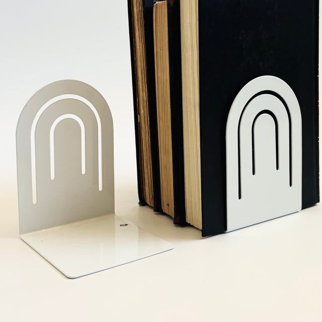 A pair of vintage postmodern metal bookends from the 1980s. Glossy white finsh in an arched shape with a perforated arched...