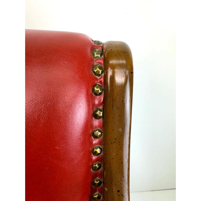 A striking mid-century armchair featuring rich red leather upholstery paired with sculpted wooden arms and tapered legs....