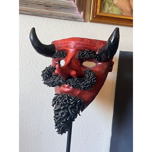 Vintage hand sculpted decorative mask representing devil. The primary red face is constructed from molded paper-mâché or...