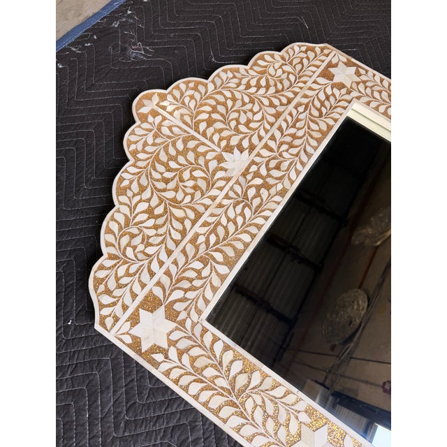 Bohemian-inspired arched mirror featuring an ivory frame with intricate gold botanical detailing and star accents. The...