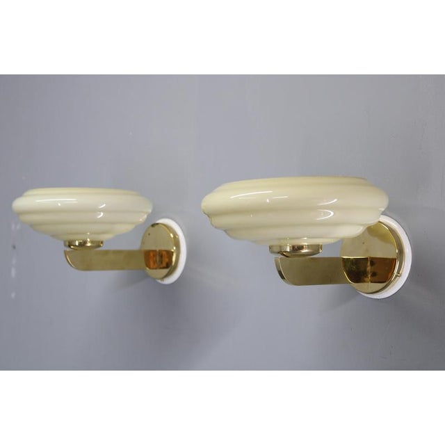 A pair of art deco wall lights produced in czechoslovakia during the 1940s, combining pressed opaline glass with brass-...