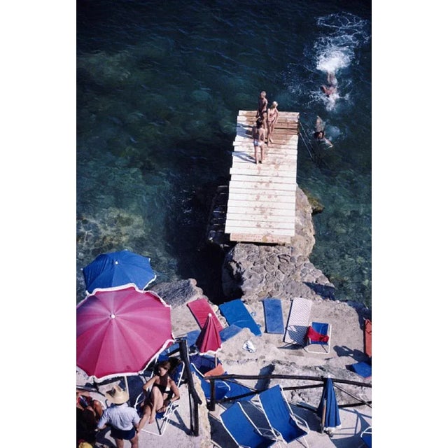 Porto Ercole 1980 by Slim Aarons Slim Aarons Limited Estate Edition A jetty juts out from a rocky shoreline in Porto...