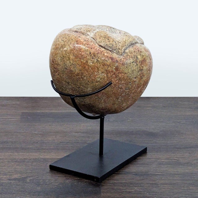 This is a natural stone sculpture is displayed on a sturdy black metal stand. The stone features warm earthy tones with a...