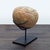 This is a natural stone sculpture is displayed on a sturdy black metal stand. The stone features warm earthy tones with a...