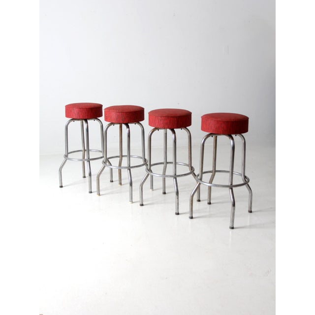 This is a set of four vintage bar stools. The single ring stools feature chrome legs with red upholstered swivel seats.