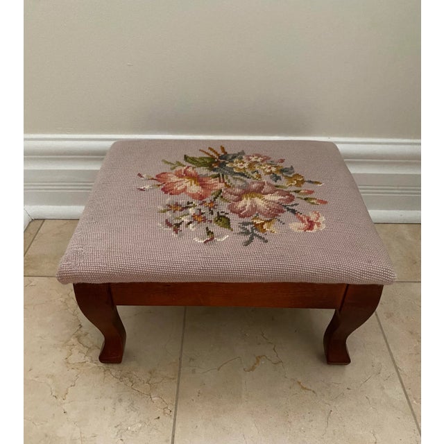 This charming mid 20th century footstool features a hand-stitched wool floral needlepoint top in soft pink with richly...