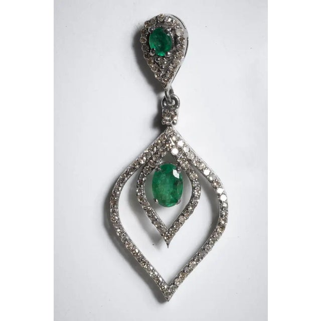A pair of emerald and diamond tear drop dangle earrings. The post and center feature large, oval faceted emeralds and...