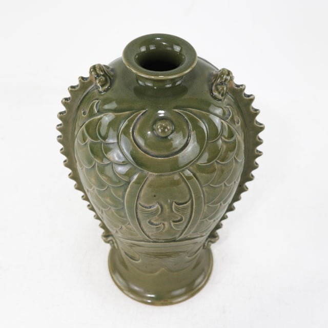 A striking Chinese celadon-glazed vase in the form of a mythical fish, featuring intricate relief carvings of scales,...