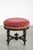 This antique English stool has been reupholstered in red fabric and features a black wooden base. The stool has casters...