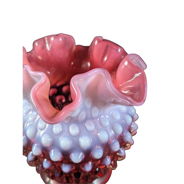 This Fenton vase is made in cranberry red with an opalescent finish and hobnail pattern. Measures 4.5 inches tall.