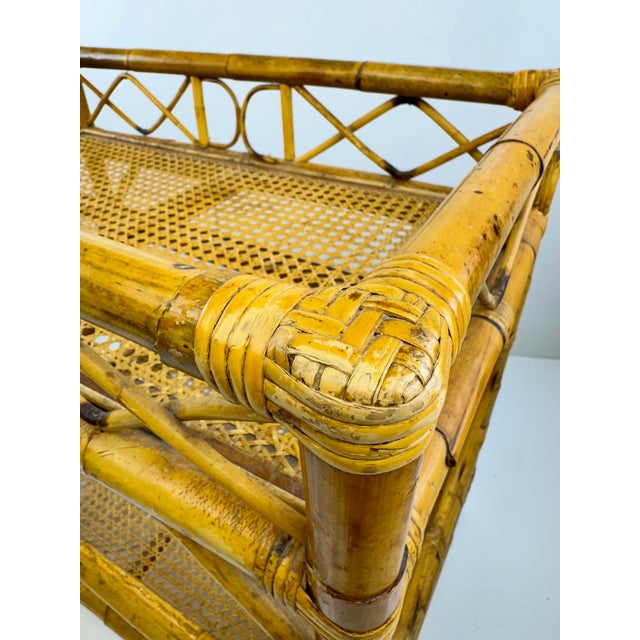 A distinctive vintage bamboo and cane bar cart featuring two woven cane shelves, decorative geometric fretwork, and a...