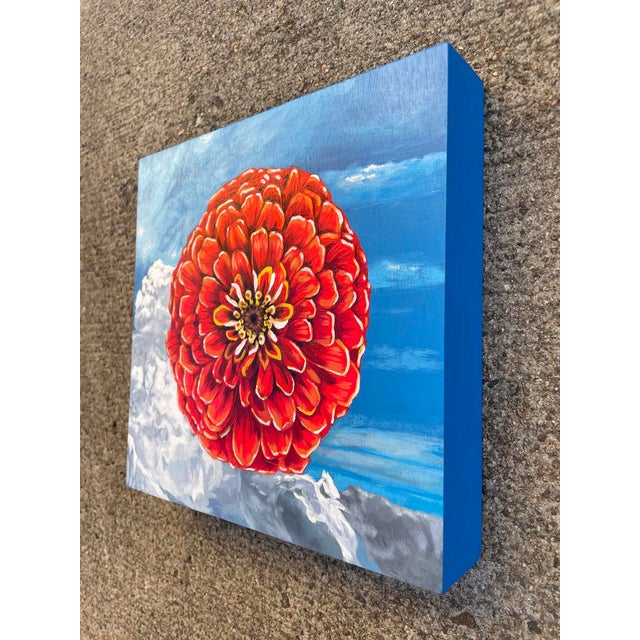 This artwork features a vibrant zinnia in bold reds and oranges, set against a striking blue sky with soft, billowing...