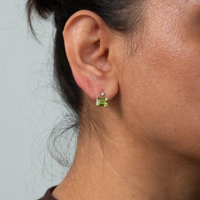 This pair of solid 14K yellow gold earrings centres two peridot stones in emerald cut, 3.36 carats together, framed by two...