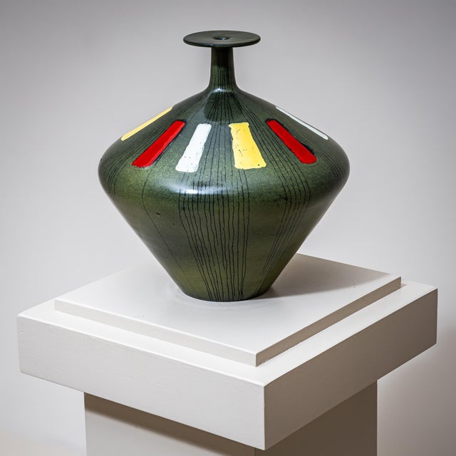 Ceramic vase with green glaze, black stripe decoration, and vertical rectangular accents in red, white, and yellow. The...