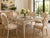 A striking vintage dining table featuring an intricately woven rattan frame in a soft ivory finish. The substantial square...