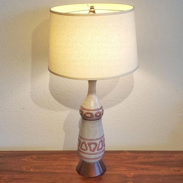 A shapely ceramic table lamp with a bubbly, light gray glaze, festooned with pink, biomorphic shapes between horizontal...