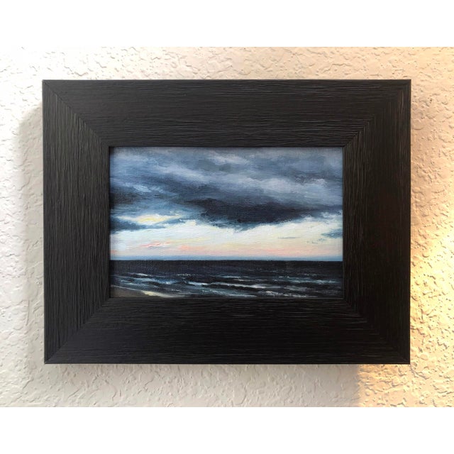 The artwork captures a dramatic coastal scene, where dark, tumultuous clouds loom over a restless sea, hinting at an...