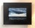 The artwork captures a dramatic coastal scene, where dark, tumultuous clouds loom over a restless sea, hinting at an...