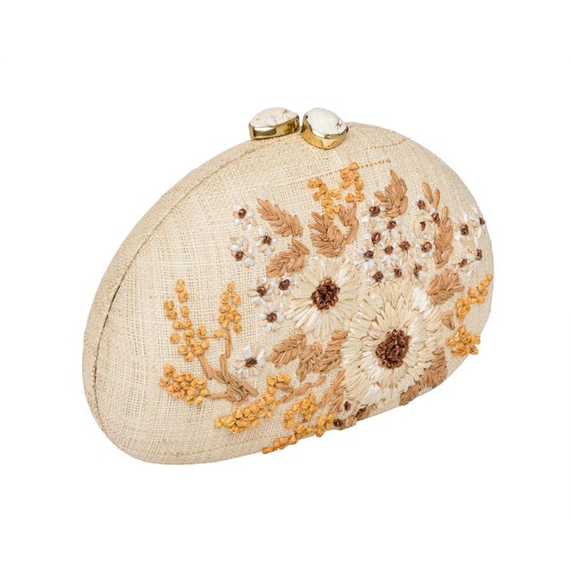 Dome clutch in natural raffia embroidered with ivory flowers. Ivory stone clasp closure. Lined with slip pocket and drop...
