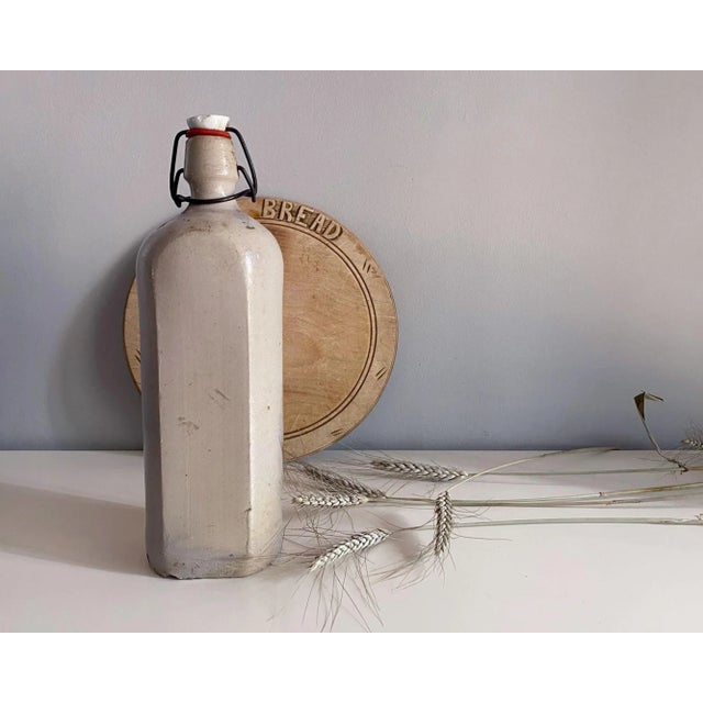 This antique stoneware bottle or jug has an unusual shape, with two flat sides, topped with an arc under the neck of the...