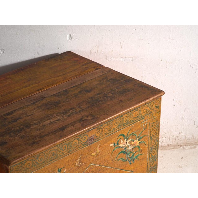 This antique Chinese painted trunk in elm wood is a dowry chest with a two-part sliding lid and a painted front. It...