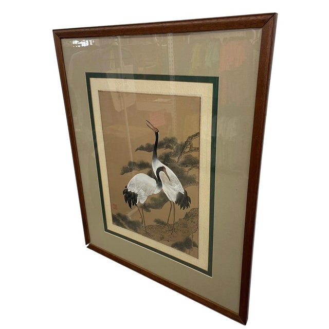 Decorative framed Asian-style artwork depicting two cranes standing on a rocky outcrop beneath pine branches. The...