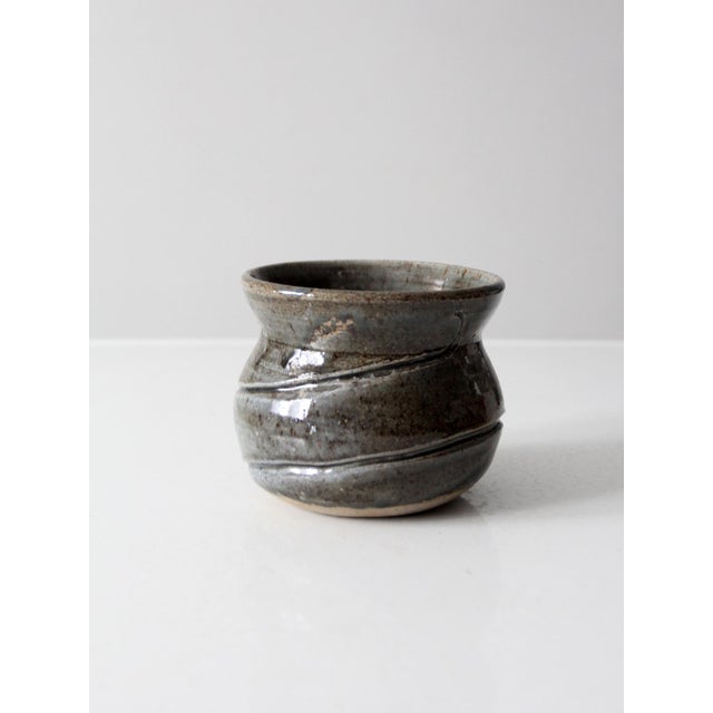A vintage studio pottery vase finished in deep grey tones with a soft cinched shape that feels balanced and sculptural....