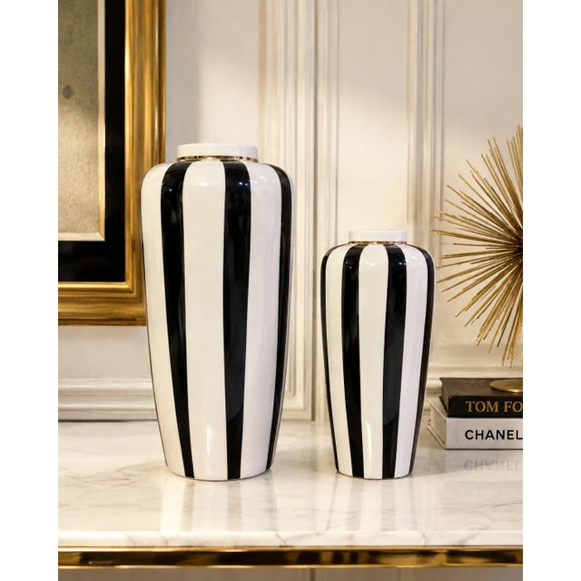 Offering a striking pair of black-and-white striped ceramic vases featuring bold vertical detailing and delicate gold-tone...