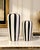 Offering a striking pair of black-and-white striped ceramic vases featuring bold vertical detailing and delicate gold-tone...