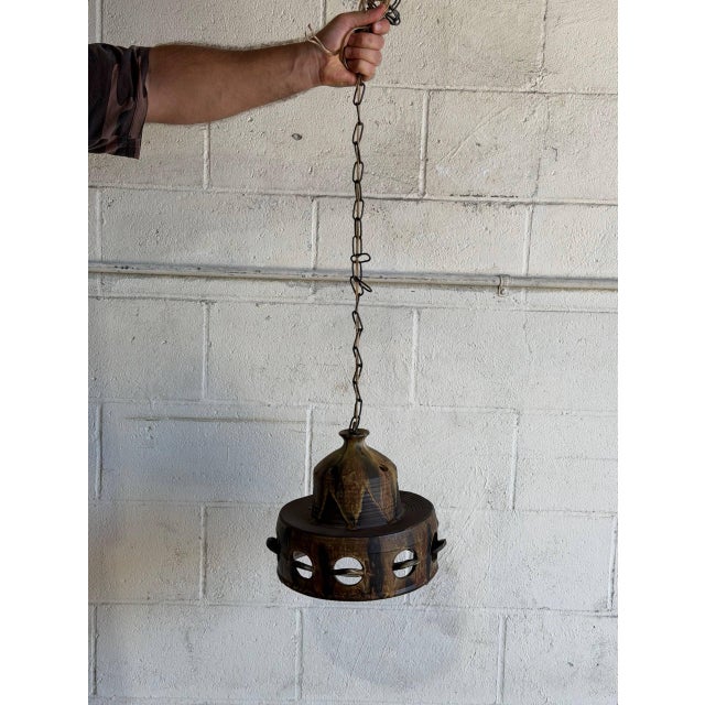 This hanging ceramic pendant lamp showcases a rich brown glazed pottery shade with unique cutout details and a suspending...