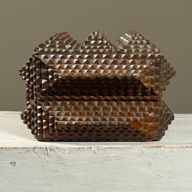 This antique lidded tramp art box is constructed in five tiers with pyramidal reliefs. The hinged lid reveals a Victorian-...