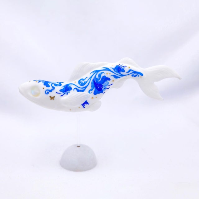 This artwork features a stylized fish, elegantly rendered in a glossy resin cast and adorned with intricate blue patterns...
