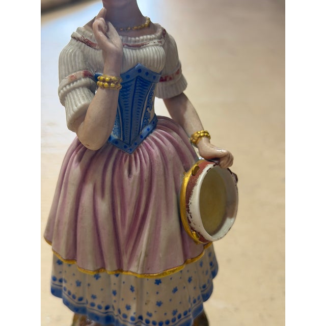 Vintage hand-painted porcelain figurine depicting a young woman in period European dress, beautifully detailed with a blue...