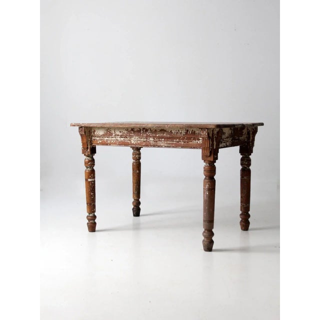 This is an antique primitive kitchen table. The rustic wooden table features chippy cream paint accents, turned legs, and...