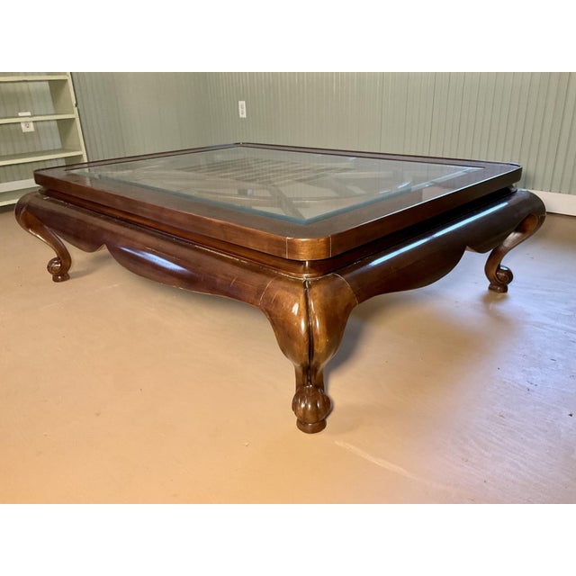 A large vintage rectangular coffee table with a rich mahogany-toned wooden frame, inset beveled glass top, scalloped...