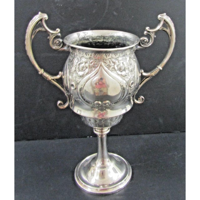 This Victorian silver plated trophy cup features intricate scroll handles and a chased floral design, adding a touch of...
