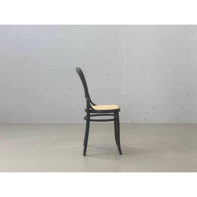 Elegant vintage bentwood chair with a black wooden frame and a light-colored cane seat. The curved design is inspired by...