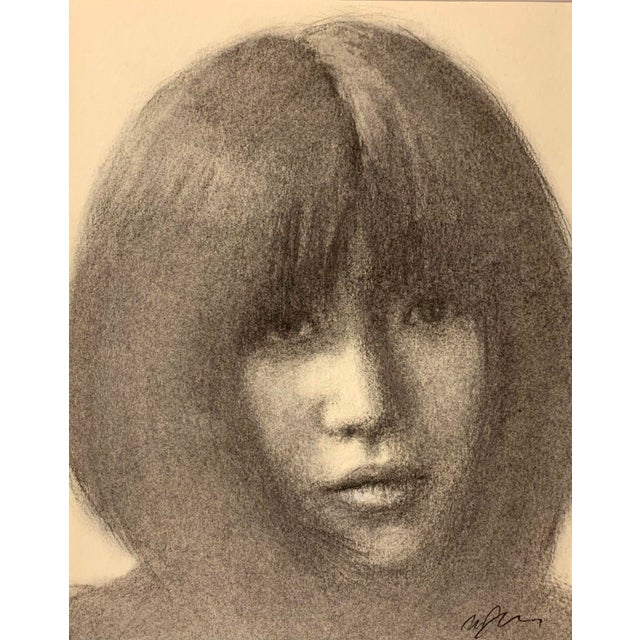 This charcoal artwork presents a close-up portrait of a figure with soft, flowing hair that frames the face, evoking a...
