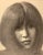 This charcoal artwork presents a close-up portrait of a figure with soft, flowing hair that frames the face, evoking a...