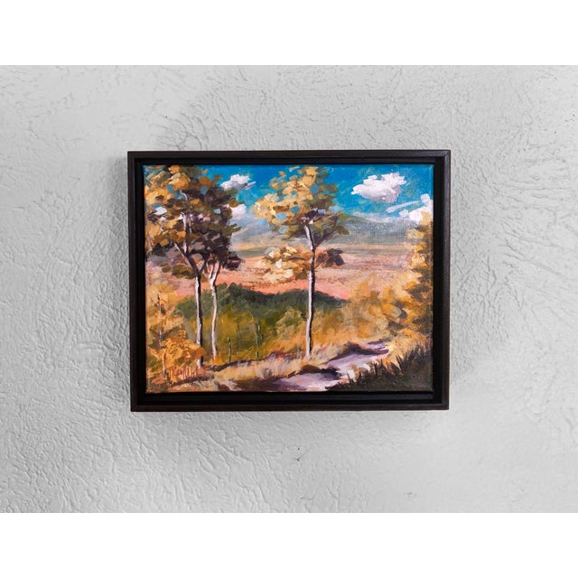 This mixed media piece captures a serene landscape, featuring tall trees with vibrant autumn foliage against a bright blue...
