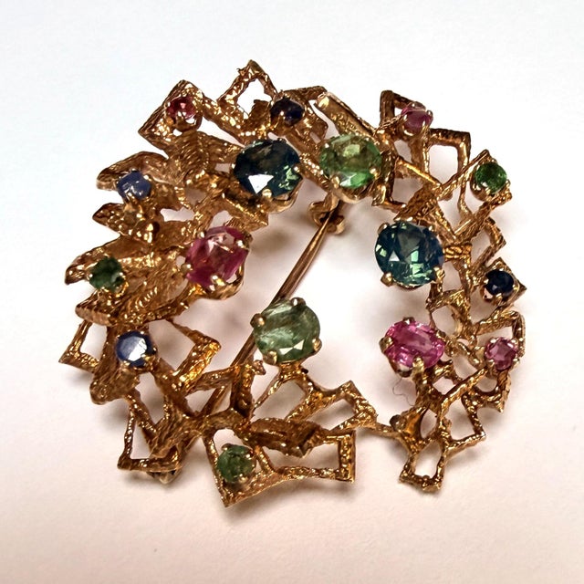 Modernist openwork brooch in 9k gold set with sapphires, pink sapphires, and emeralds (Diameter: approximately 4.2 cm)....