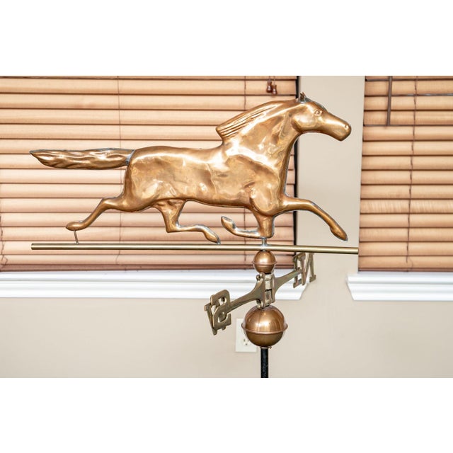 A decorative vintage copper galloping horse weathervane mounted on heavy black iron stand with brass directional arms...