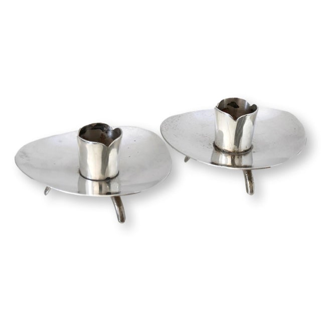 A petit sculptural pair of handcrafted Mexican sterling silver candlesticks in the Modernist style. Raised on three arched...