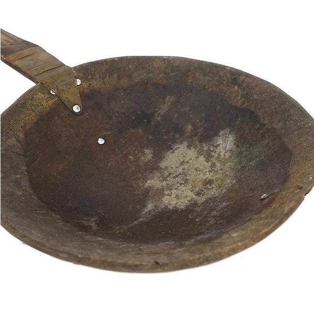 A large spoon or scoop made out of wood carved with a large bowl and a long handle with aluminum designs. This spoon is...
